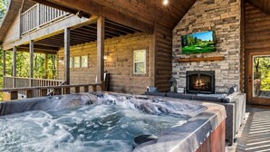Een hottub met een stenen openhaard, een houten terras en een aan de muur bevestigde televisie.