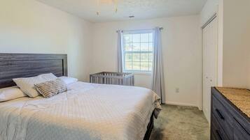 A bedroom with a bed, a crib, a window with curtains, and a ceiling fan.