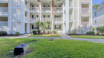 A multi-story building with balconies, a well-maintained lawn, and a pathway leading to the entrance.