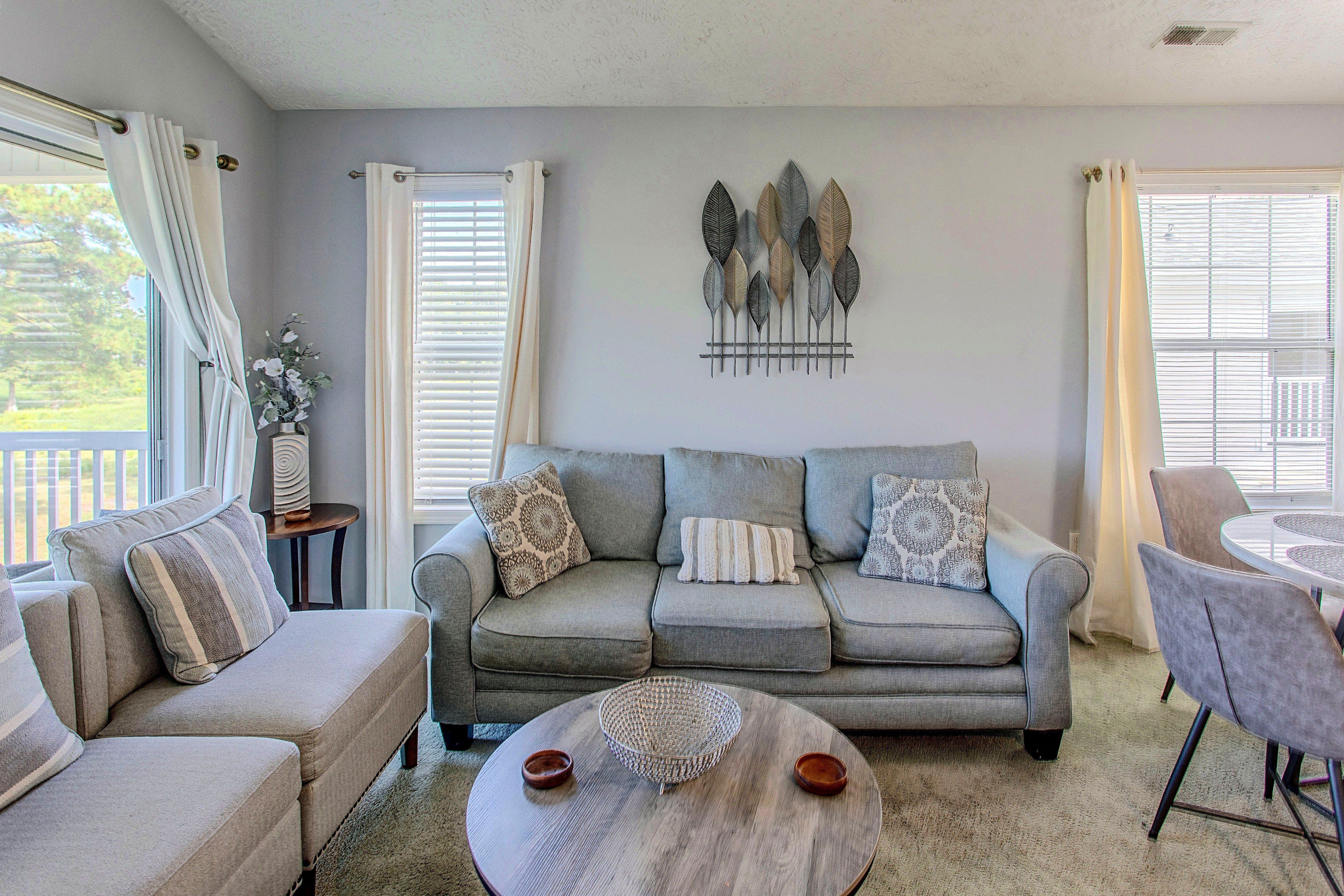 A living room with a grey sofa, two armchairs, a coffee table, and a wall-mounted art piece.