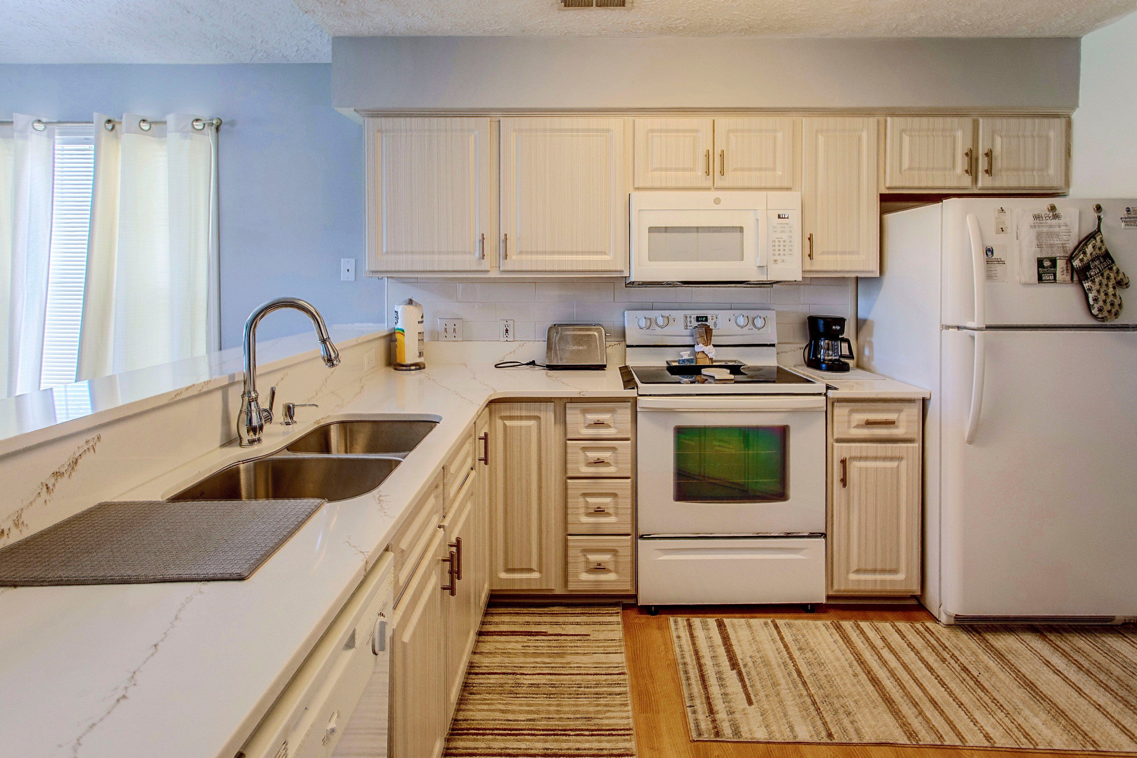 A kitchen with white cabinets, a microwave, a stove, a sink, and a refrigerator.