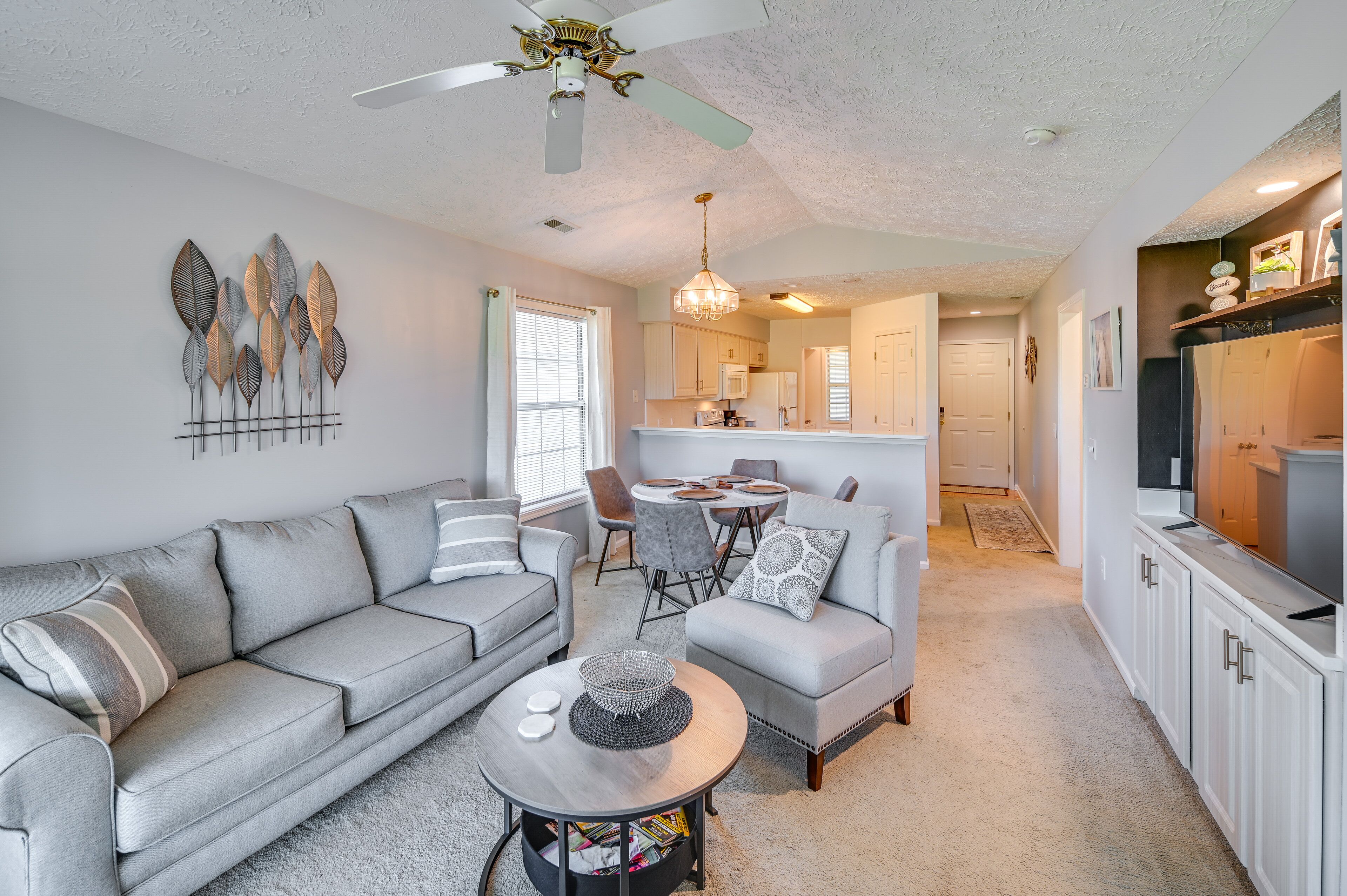 A living room with a grey sofa, a coffee table, and a dining area with a chandelier.