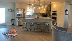 A modern kitchen with stainless steel appliances, a central island with bar stools, pendant lighting, and a large window providing natural light.