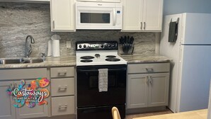 A kitchen with white cabinets, a white microwave, a stove, a sink, and a refrigerator. - Peaceful Island Living @ The Buccaneer Condo 1BR/1 BR with pool and dock (Saint James City)