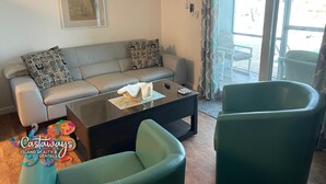 A living room with a grey sofa, patterned cushions, a coffee table, and two green armchairs. - Peaceful Island Living @ The Buccaneer Condo 1BR/1 BR with pool and dock (Saint James City)