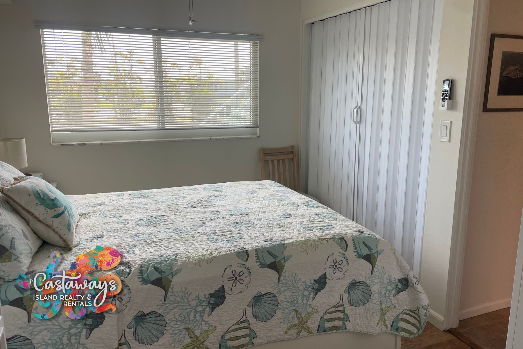A bedroom with a bed, a window with blinds, a chair, and a door with a curtain.