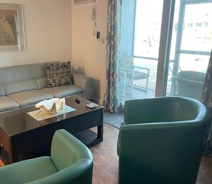 Un salon avec un canapé gris, des coussins à motifs, une table basse et deux fauteuils verts.
