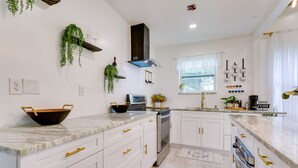 Una cocina moderna con armarios blancos, tiradores dorados y encimera de mármol.