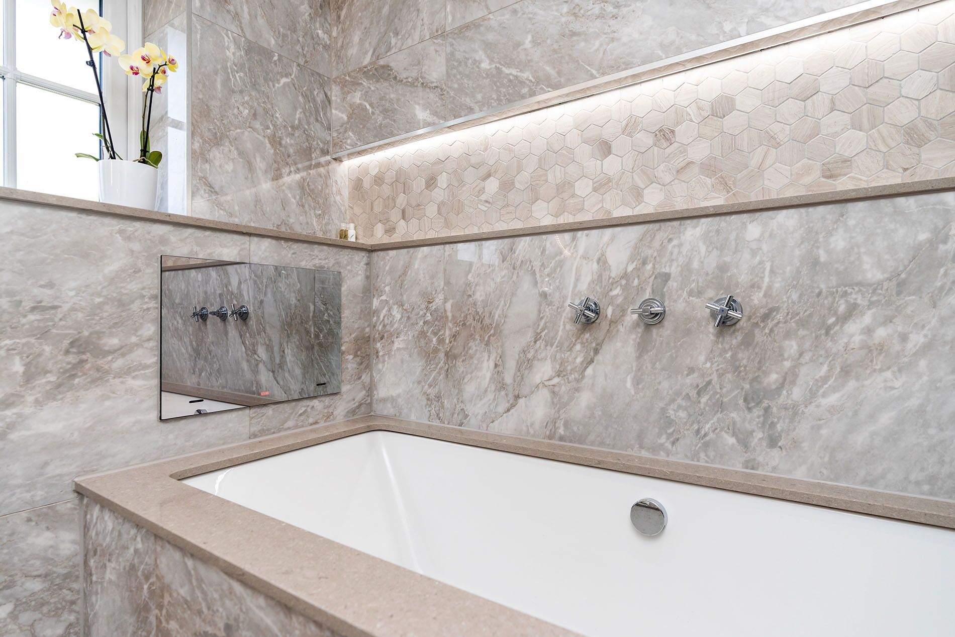 Ein modernes Badezimmer mit Marmorwand, einer großen Badewanne und einem Spiegelunterschrank.