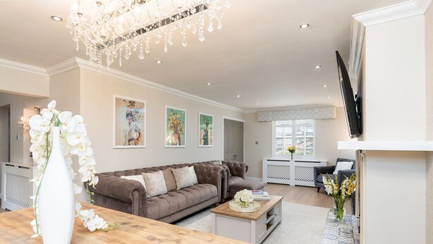 A spacious living room with a brown sofa, a wooden coffee table, and a white vase with flowers. There are framed artworks on the wall and a chandelier above. - New Listing Special Discount! (Greater Manchester)