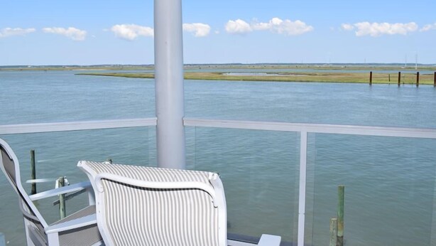 A balcony with a view of a calm body of water and distant land. - Sunset Bay Villa #202- Waterfront, In Town, Pool & Gym (Chincoteague)