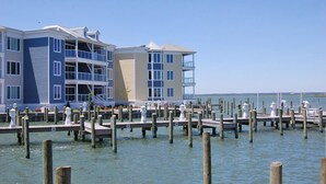 A waterfront property with multiple balconies, a dock extending into the water, and a clear view of the sea. - Sunset Bay Villa #202- Waterfront, In Town, Pool & Gym (Chincoteague)