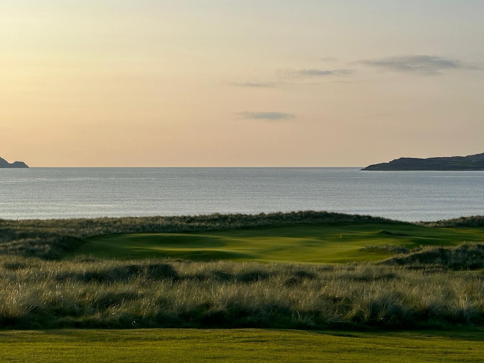 A golf course with a view of the sea and distant hills.