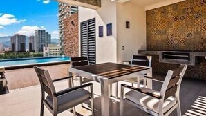 A modern outdoor patio with a pool view, a dining table with chairs, and a patterned wall. - A FEW BREEZY STEPS TO THE BEACH ~LUXURIOUS STAY~ (Puerto Vallarta)