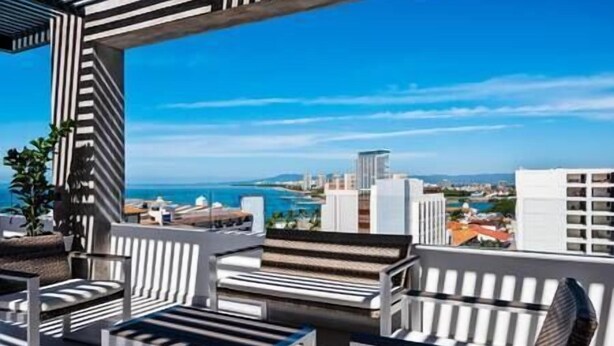 A rooftop terrace with striped seating and a view of the city and sea. - A FEW BREEZY STEPS TO THE BEACH ~LUXURIOUS STAY~ (Puerto Vallarta)