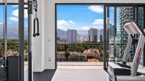 A modern gym with a treadmill, weights, and a large window offering a city view. - A FEW BREEZY STEPS TO THE BEACH ~LUXURIOUS STAY~ (Puerto Vallarta)