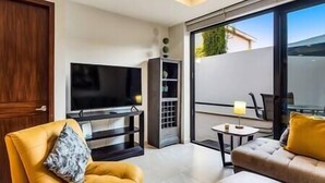 A modern living room with a flat-screen TV, a sofa, a chair, and a small table. - A FEW BREEZY STEPS TO THE BEACH ~LUXURIOUS STAY~ (Puerto Vallarta)