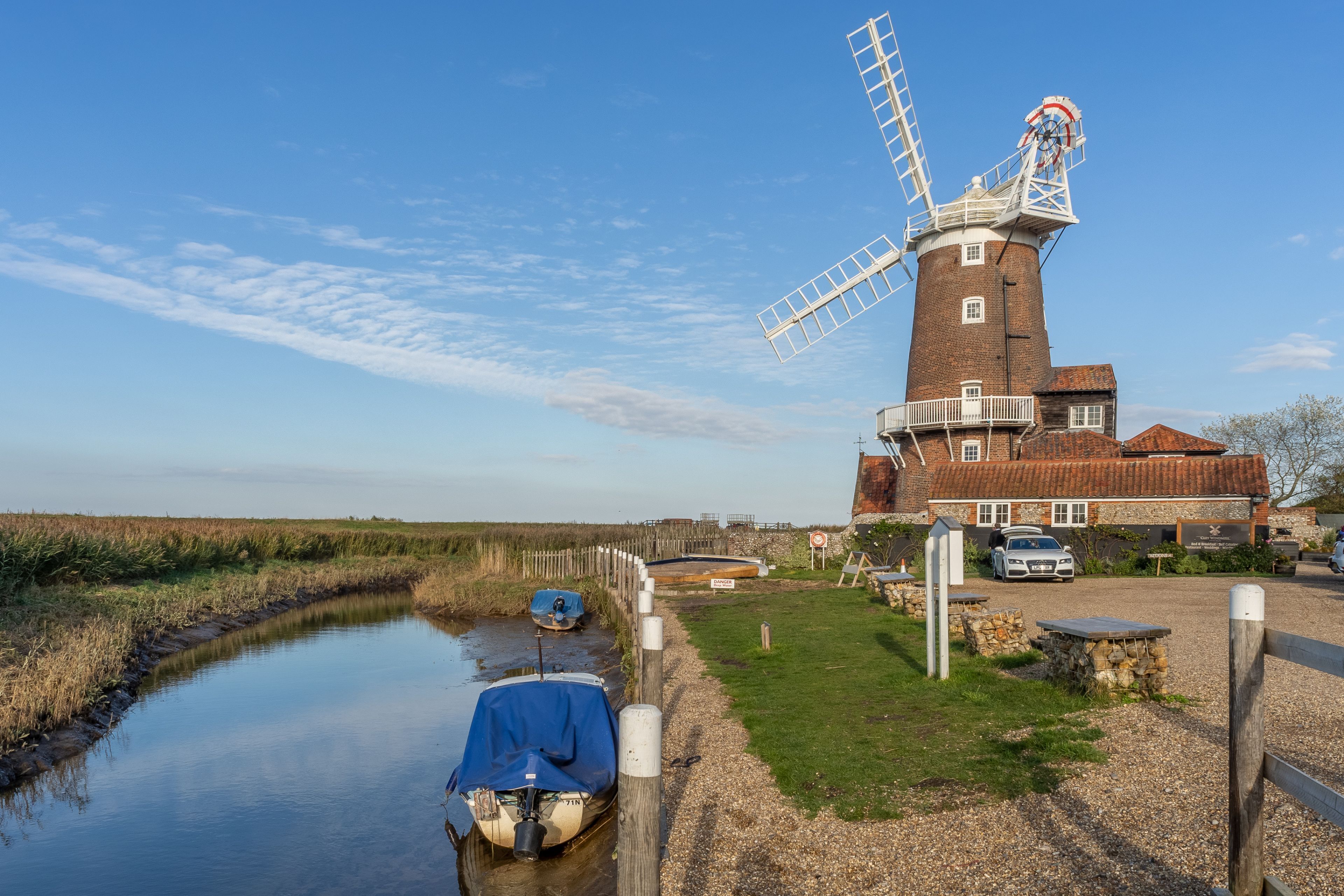 A windmill with a gravel path and a small boat docked by the water.
