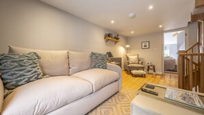 A modern living room with a beige sofa, patterned cushions, a small side table, and a wooden staircase.