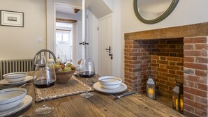 A dining area with a wooden table set for a meal, a brick fireplace, and a view into another room.