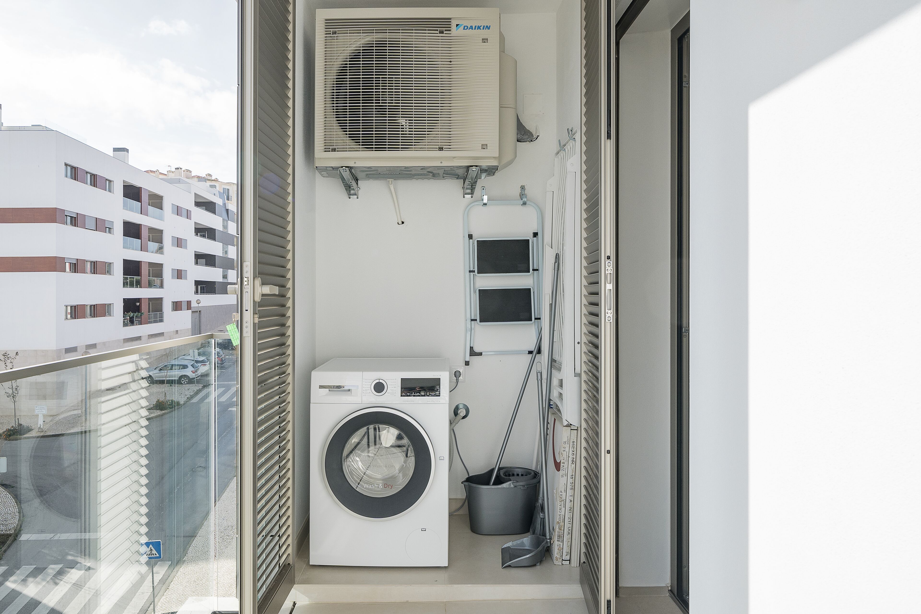 Een ruim balkon met een wasmachine, een droogrek en een airconditioning.