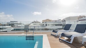 Een zwembad op het dak met helderblauw water, een glazen balustrade en ligbedden.
