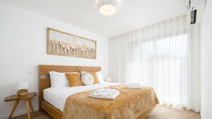 Een netjes ingerichte hotelkamer met een groot bed, een nachtkastje, een kunstwerk aan de muur en dunne gordijnen die natuurlijk licht doorlaten.