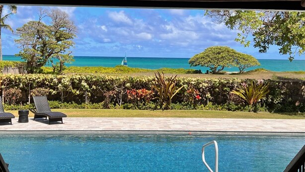 Zona de piscina con vista al océano y un velero.