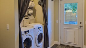A laundry room with two front-loading washers and dryers, a white door with a window, and a beige rug on the floor.