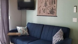 A living room with a blue sofa, a small side table, a mounted TV, and a botanical print on the wall.