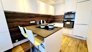 Eine moderne Küche mit weißen Schränken, einer Holzwand als Blickfang, Edelstahlgeräten und einer zentralen Kochinsel mit Hockern.
