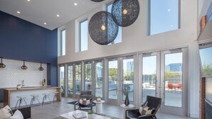 A spacious living area with a sofa, coffee table, and chairs, large windows, and a kitchen area with bar stools.