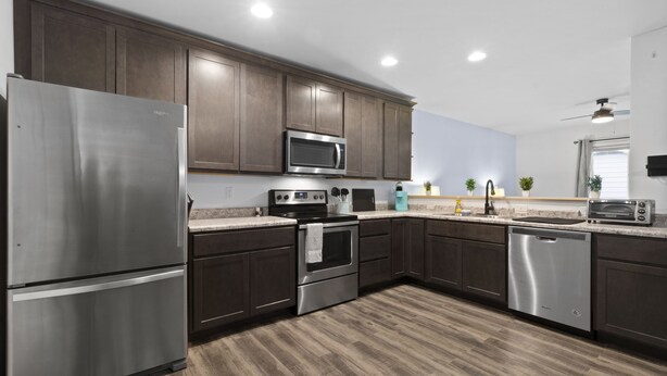 A modern kitchen with dark wood cabinets, stainless steel appliances, and a wooden floor. - Modern Studio Apartment in the heart of Festus (Festus)