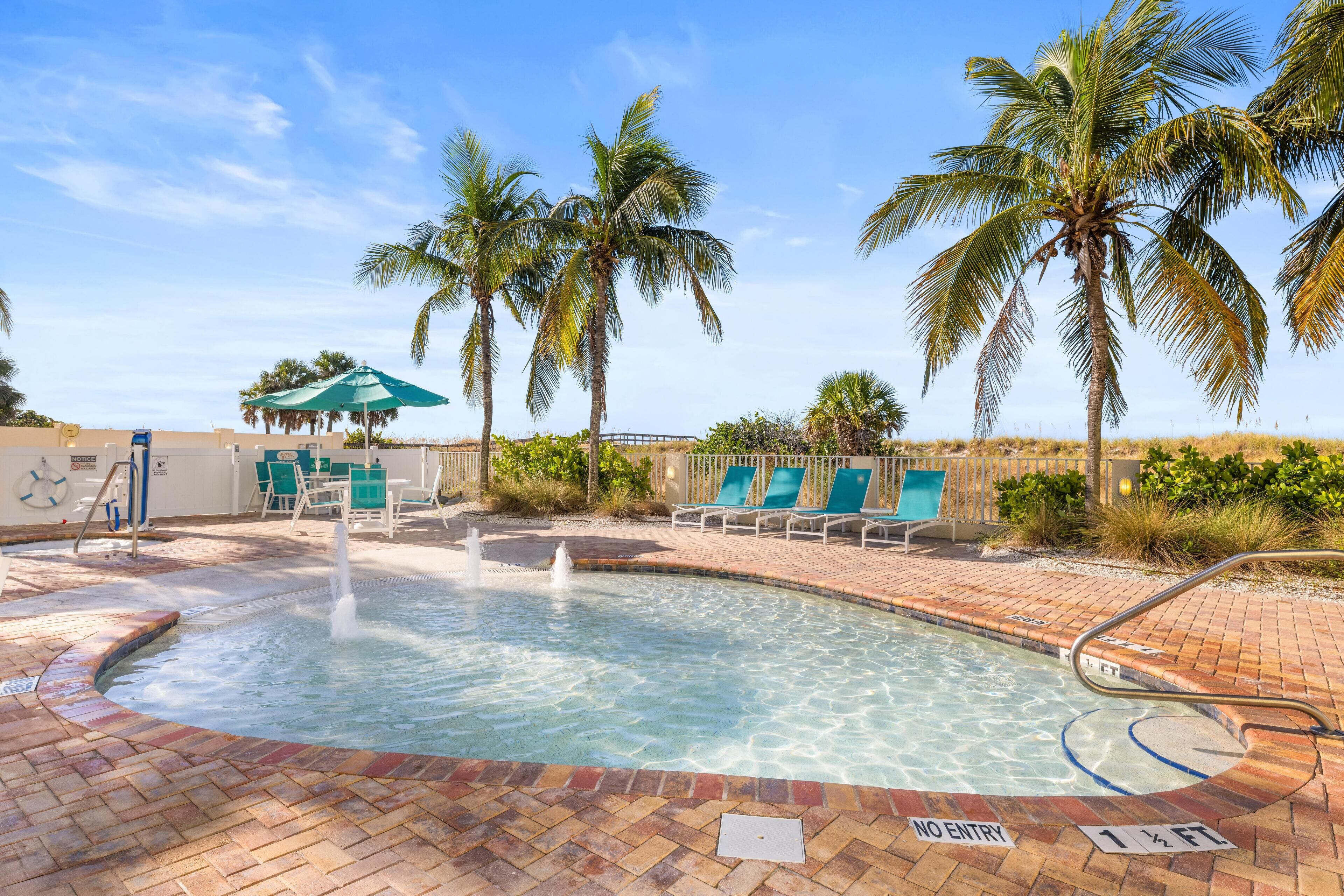 A swimming pool with a no entry sign, lounge chairs, palm trees, and a brick pathway.