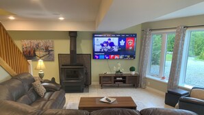 A living room with a fireplace, a television displaying sports, and a view of the outdoors. - Viceroy home at Soames Hill (Gibsons)