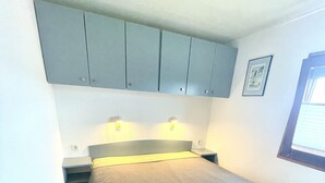 A small, compact bedroom with a single bed, a nightstand, a wardrobe, and a window with blinds. - Mobilheim an der Ostsee, 350 m zum Strand (Heringsdorf)
