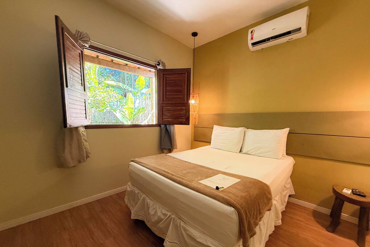 Une chambre d’hôtel avec un lit, une fenêtre avec des rideaux, un appareil de climatisation et une petite table.