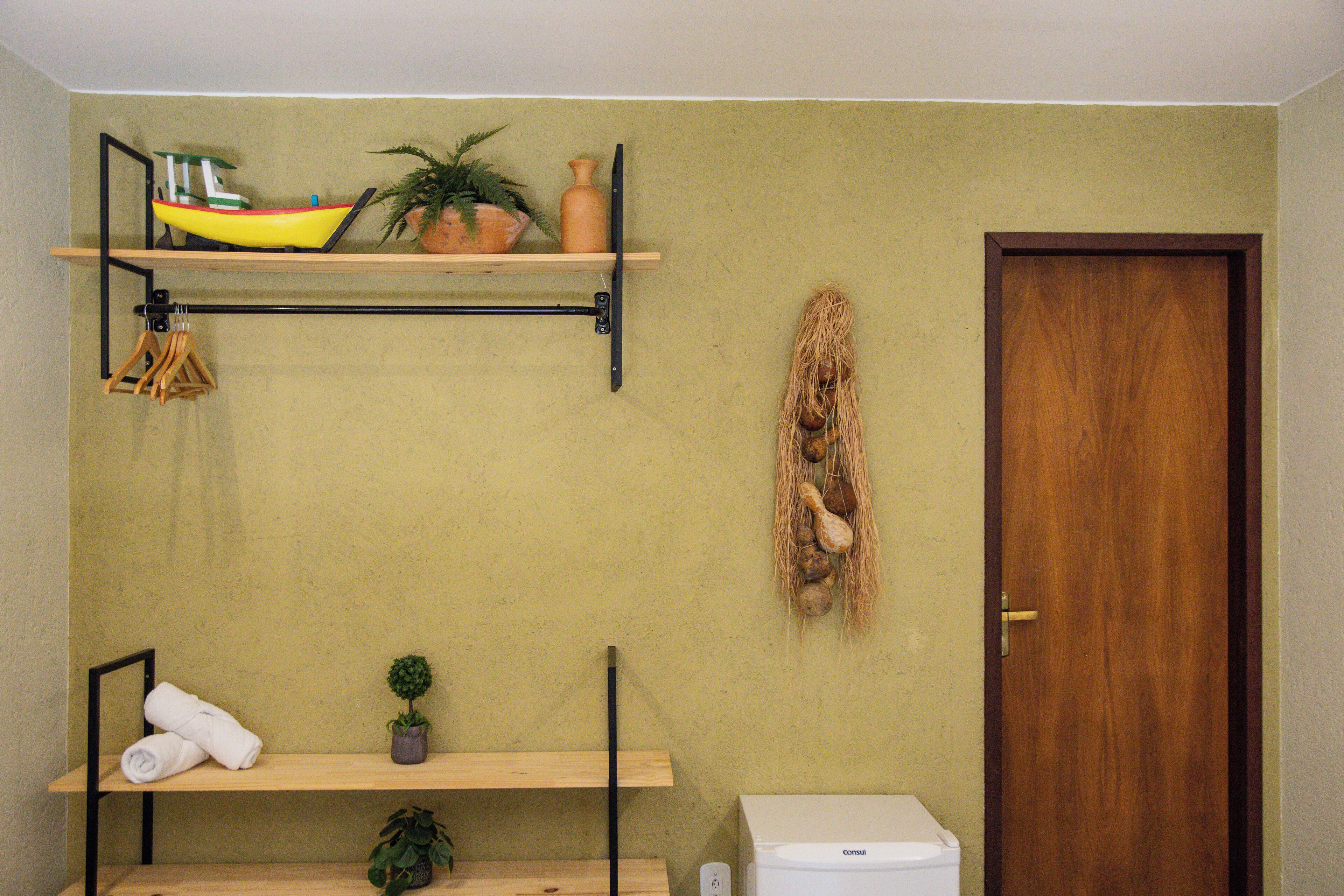 Baño con repisa de madera que sostiene un modelo de barco amarillo, una planta en maceta y un adorno colgante de nido. Hay un inodoro, una toalla y una planta pequeña en una repisa inferior.