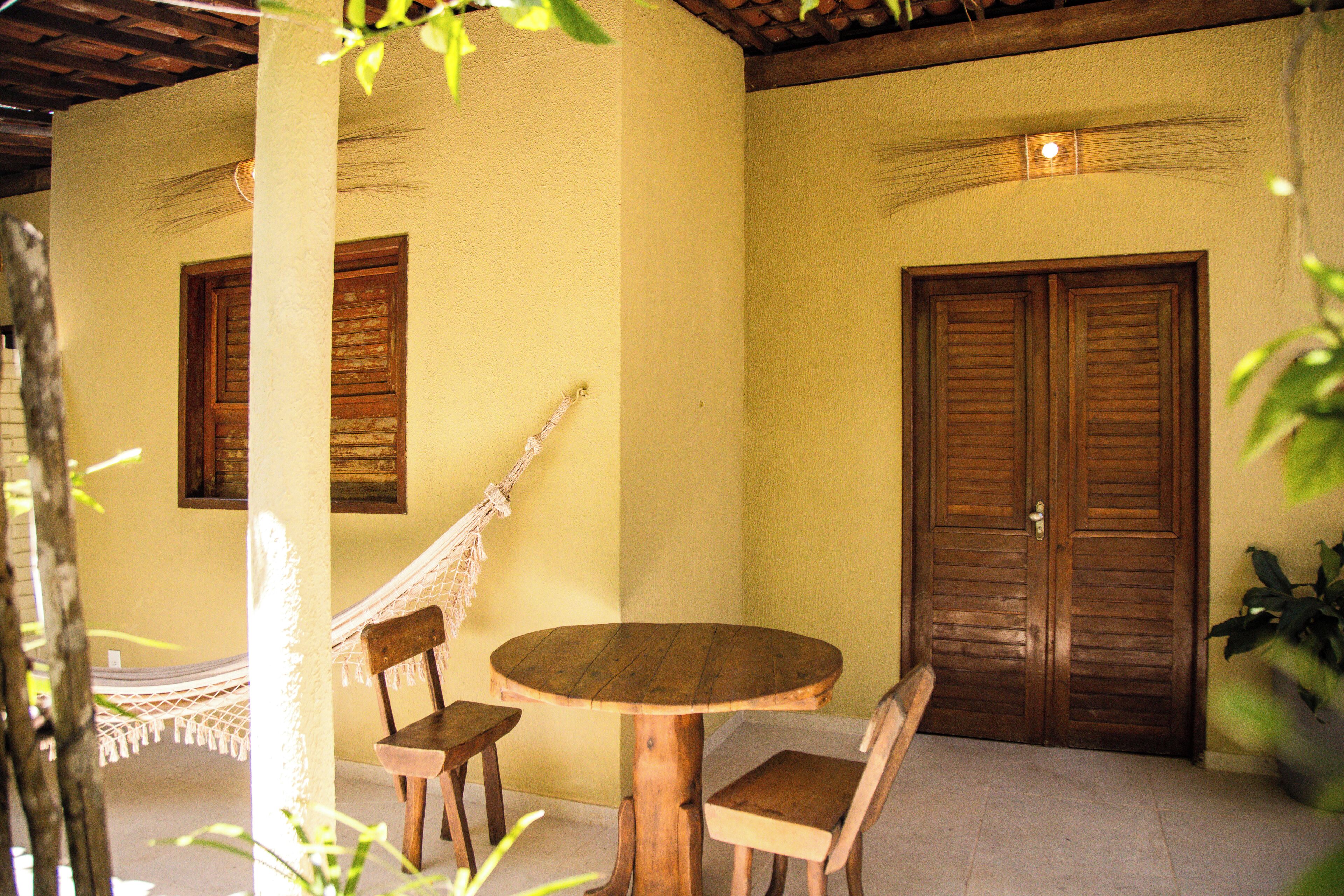 A wooden table with chairs, a hammock, and a door in a room with yellow walls.