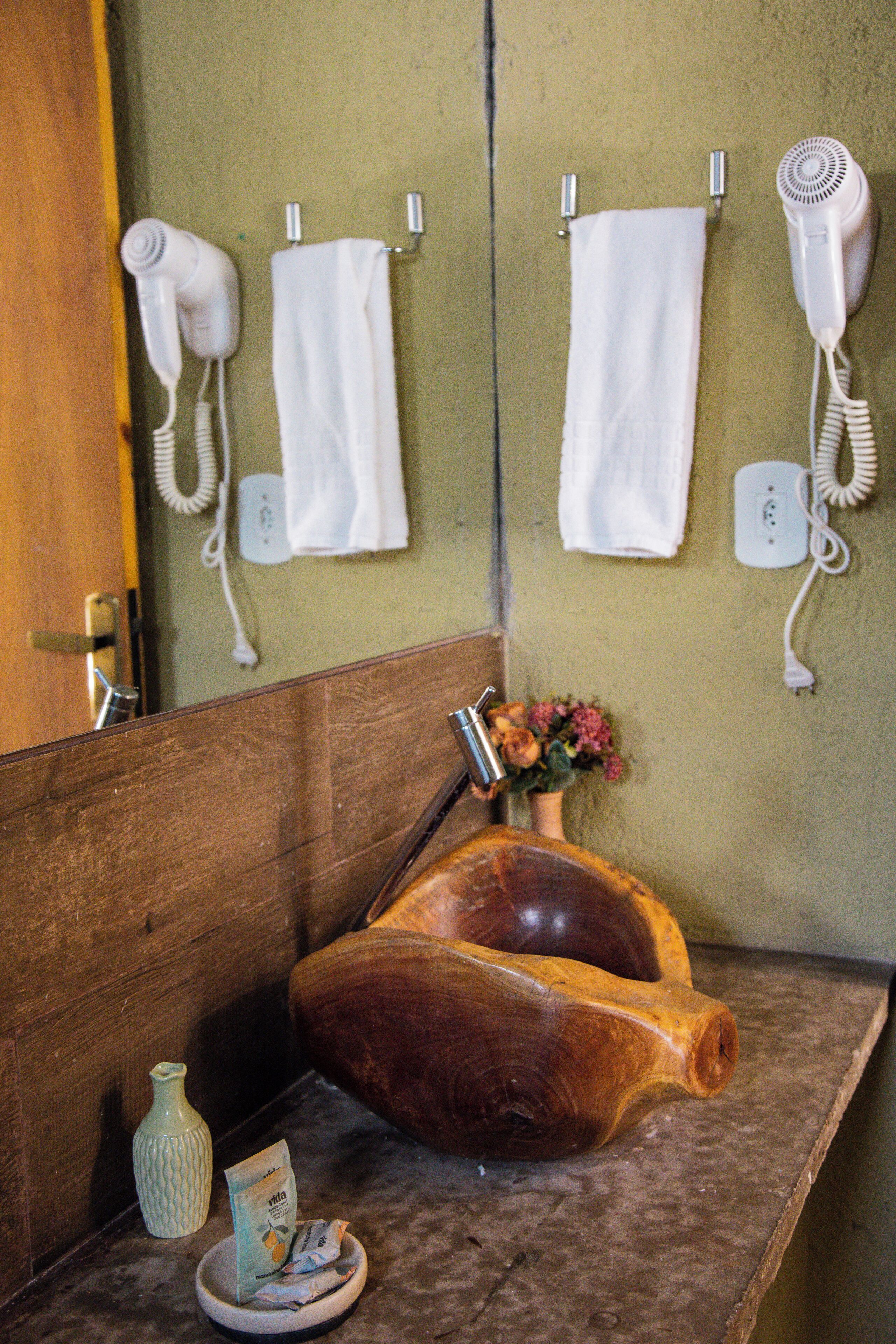 Ein Badezimmer mit einem Holzbac, einer Vase mit Blumen und zwei an der Wand befestigten Haartrocknern.