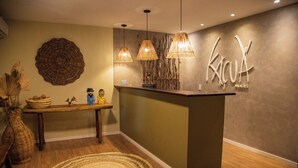 A reception area with a wooden reception desk, wicker pendant lights, a woven wall decoration, and a textured rug. - Pousada kaçuá Milagres (São Miguel dos Milagres)