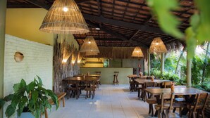 A restaurant with wooden tables and chairs, hanging bamboo lamps, and a brick wall. - Pousada kaçuá Milagres (São Miguel dos Milagres)