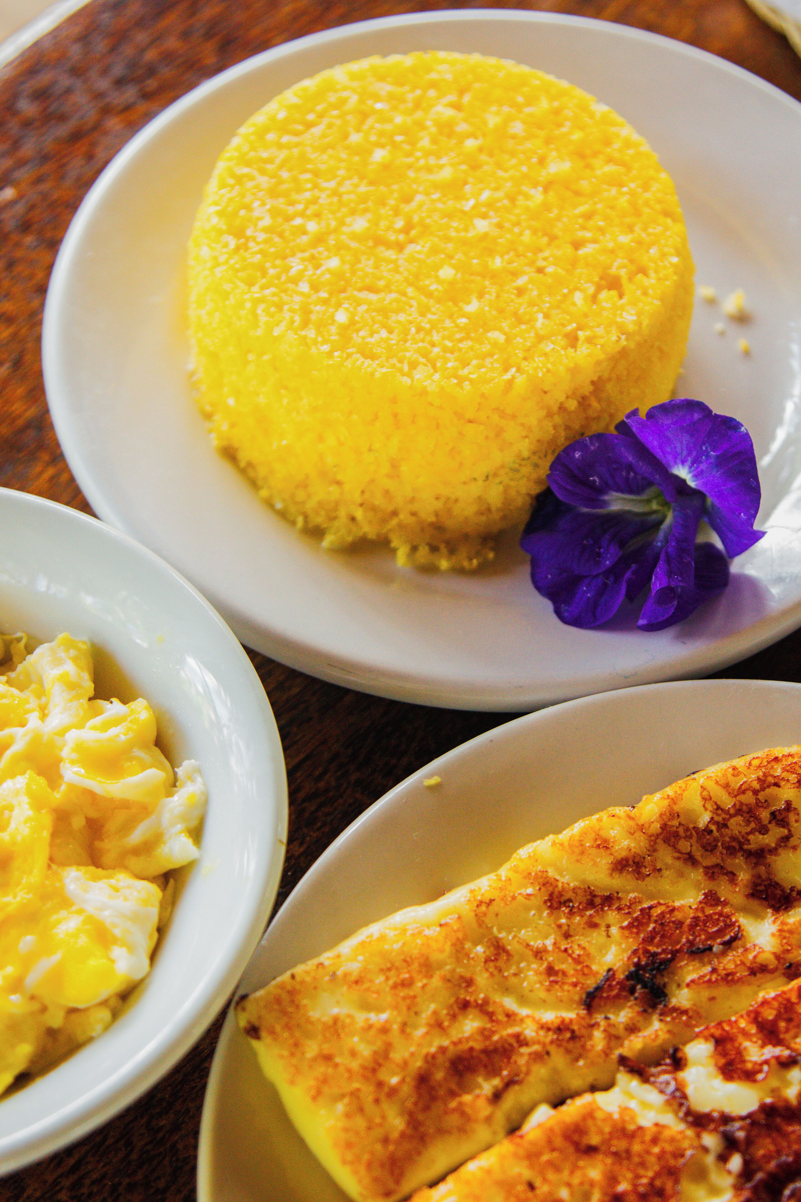 A plate of yellow food, possibly a dessert, with a purple flower on it.