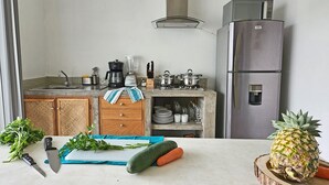 A kitchen with a sink, stove, microwave, and refrigerator. There are vegetables on the counter and a pineapple on a wooden board. - 2BR - Fast Internet, Near Beach, Pool, King Beds, ACs (Puerto Escondido)