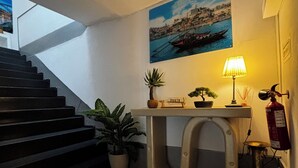 Eine Treppe führt zu einer Empore mit Tisch, Pflanzen, einer Wandlampe und einem Gemälde einer Küstenlandschaft.