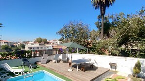 Ein Poolbereich auf dem Dach mit einer Holzterrasse, Liegestühlen und einem Tisch.