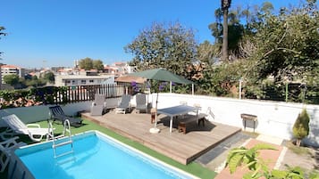 A rooftop pool area with a wooden deck, lounge chairs, and a table.