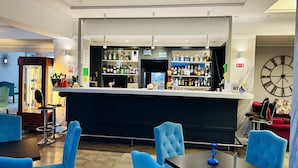 A bar area with a counter, shelves of bottles, and blue upholstered chairs. - Alga Baltic Resort (Swinoujscie)