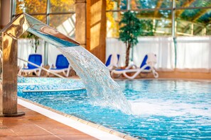 Piscina interna com água cristalina, um elemento decorativo em metal e cadeiras de lounge ao fundo.