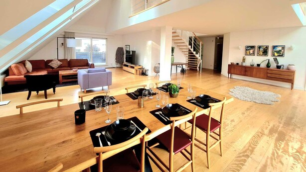 En rummelig loftlejlighed med spiseplads, opholdsstue og trappe op til en etage.